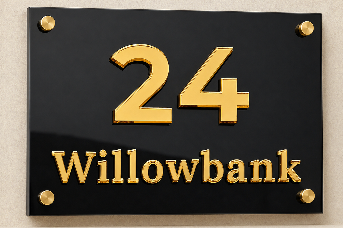 A rectangular black house number plaque with raised gold numerals '24' and the word 'Willowbank' below, mounted on a beige wall with four gold screws.lumorastudio.ie lumora craft studio