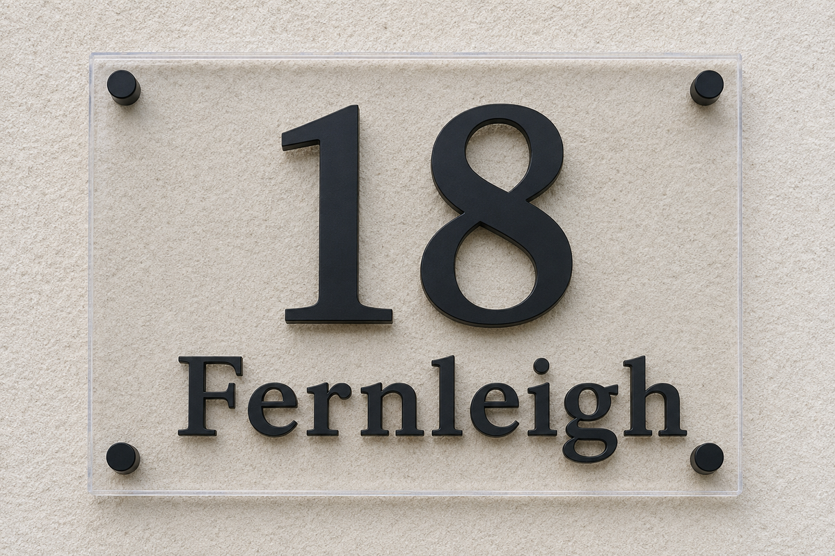 A modern house number sign displaying '18 Fernleigh' in black raised letters on a clear rectangular acrylic plaque, mounted on a textured beige stucco wall.