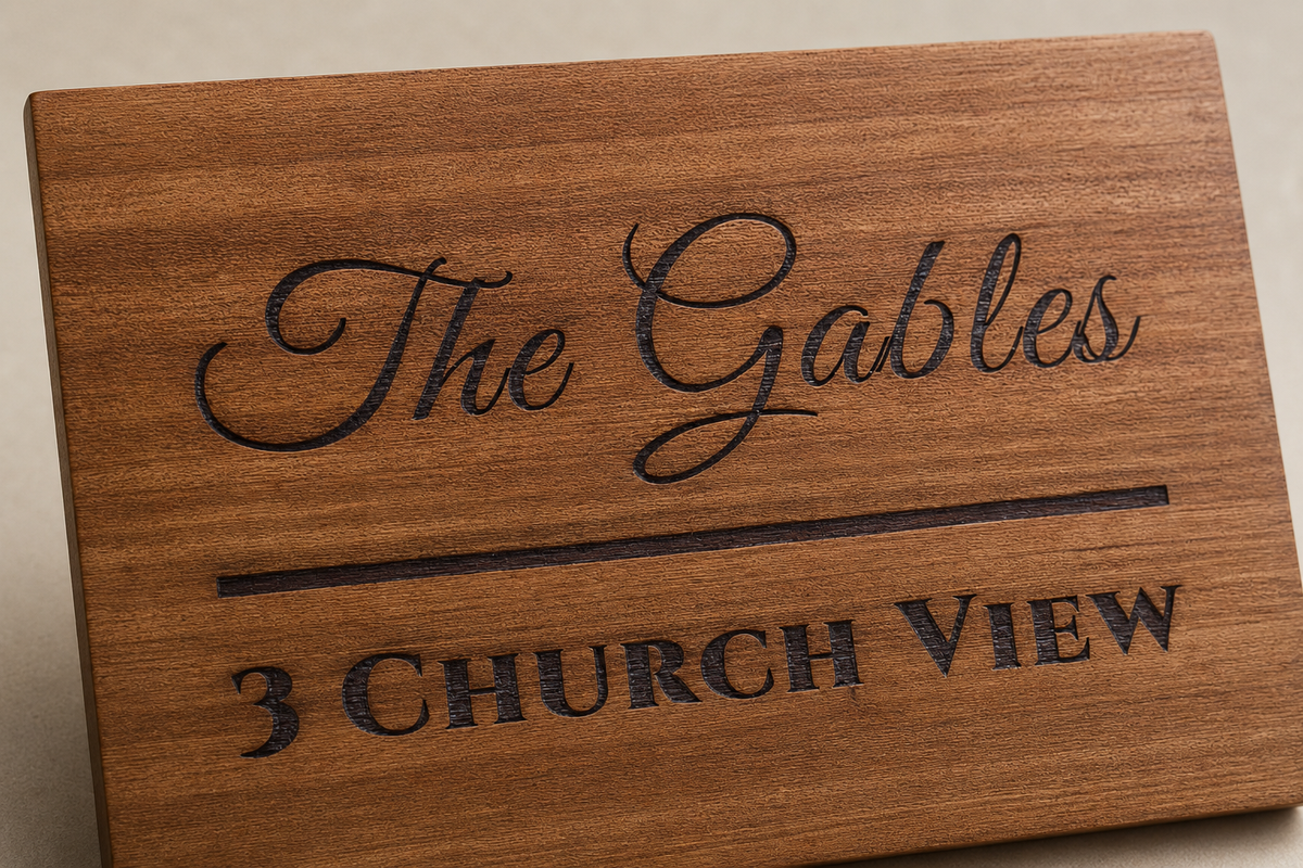 A rectangular wooden sign with engraved text reading 'The Gables' and '3 CHURCH VIEW' on a warm medium-brown wood surface.lumorastudio.ie lumora craft studio