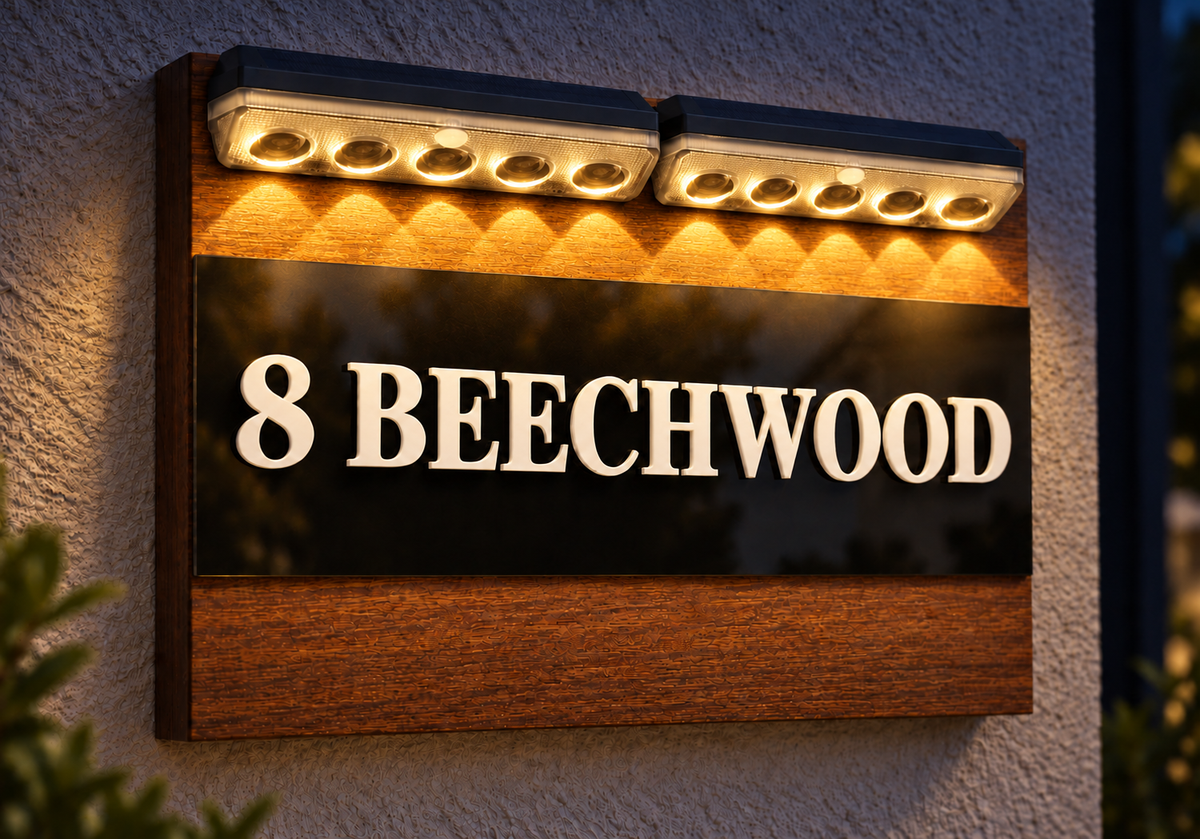 A custom wooden house sign with the text '8 BEECHWOOD' in raised white letters on a black background, mounted on a textured stucco wall. The sign features a dark wood frame, a black center panel, and a warm wood-grain lower section, illuminated by two rectangular LED light bars mounted at the top.lumorastudio.ie lumora craft studio