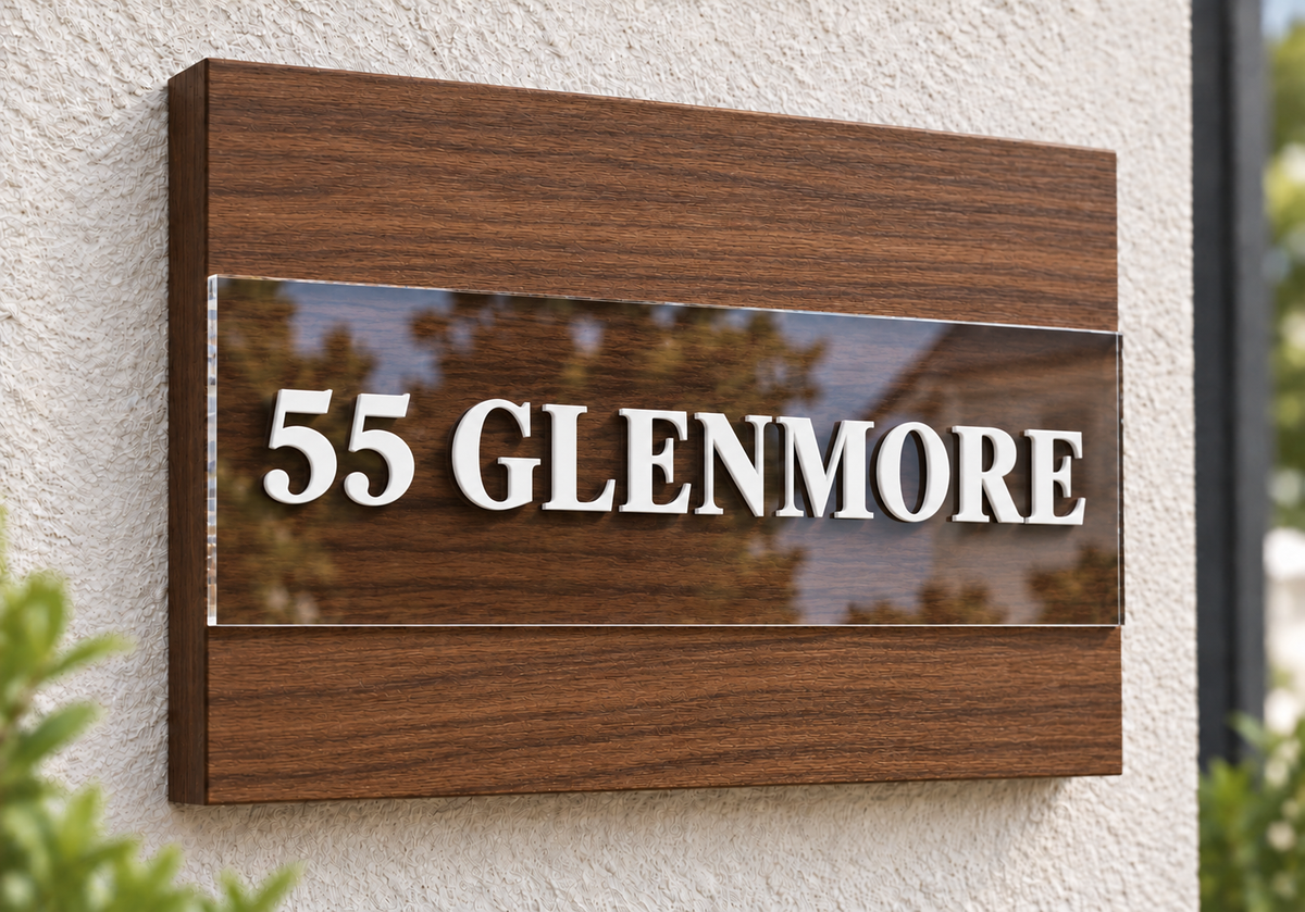A modern wooden house sign with a glossy dark brown wood-grain frame and a clear acrylic center panel displaying the white raised text '55 GLENMORE' against a textured off-white stucco wall.lumorastudio.ie lumora craft studio