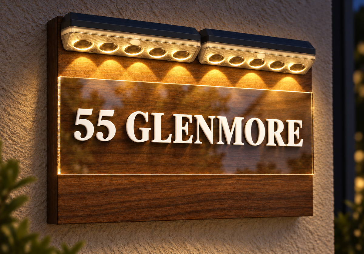 A custom outdoor LED house sign displaying '55 GLENMORE' in raised white letters over a warm wood-grain panel, mounted on a textured stucco wall with integrated solar-powered uplighting.lumorastudio.ie lumora craft studio