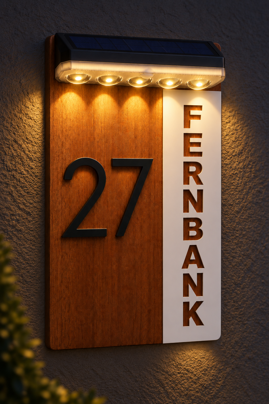 A modern house number and street name sign mounted on a textured gray wall. The sign features a vertical wood-grain panel with the number '27' in black, next to a white vertical panel with 'FERNBANK' in brown letters.Lumora Craft Studio, lumorastudio.ie