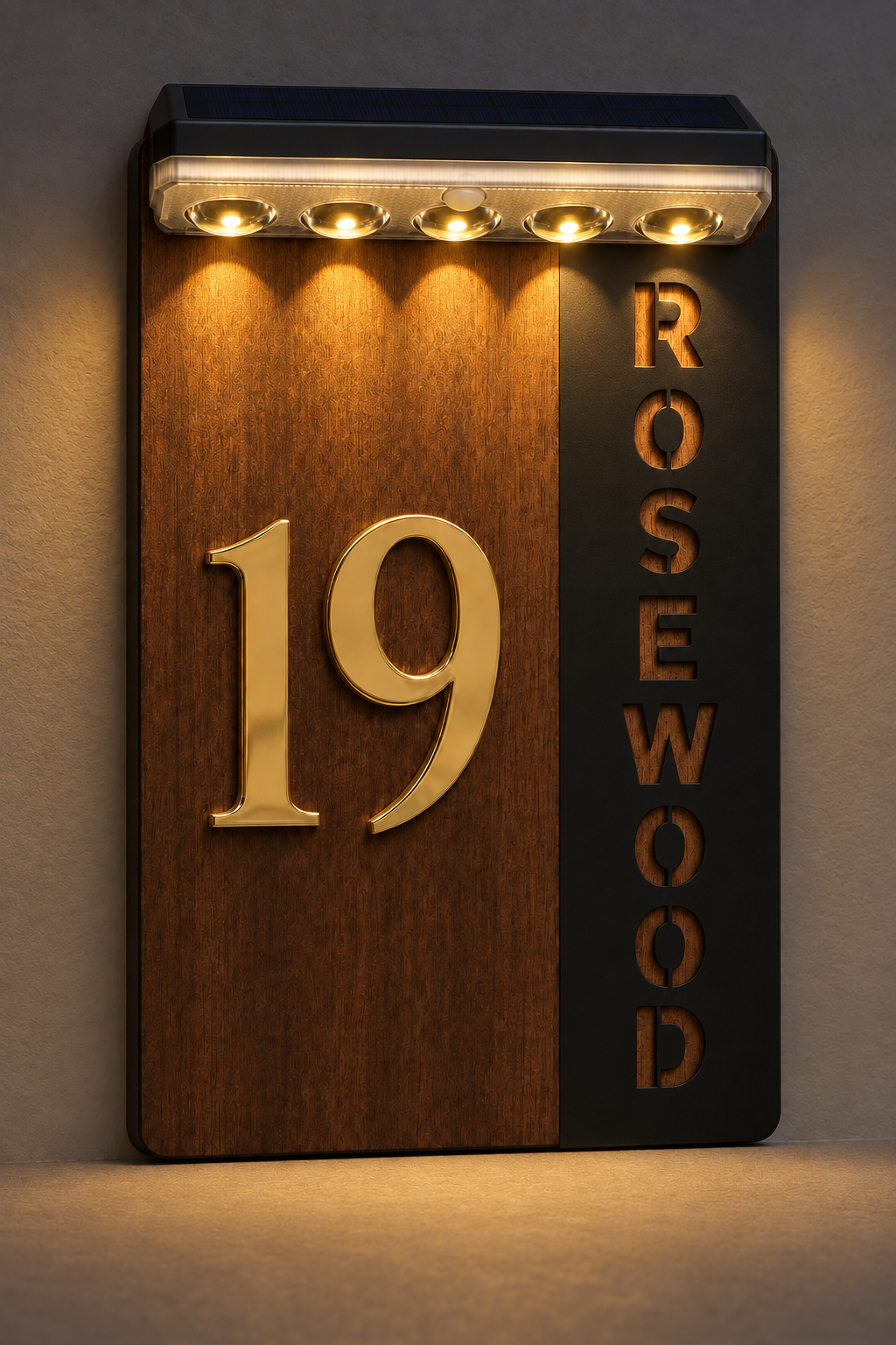 A vertical house number and name wall sign with a woodgrain panel showing the number 19 in gold, a black panel with the name ROSEWOOD in gold letters, and a built-in light bar at the top casting light onto the wall.Lumora Craft Studio, lumorastudio.ie
