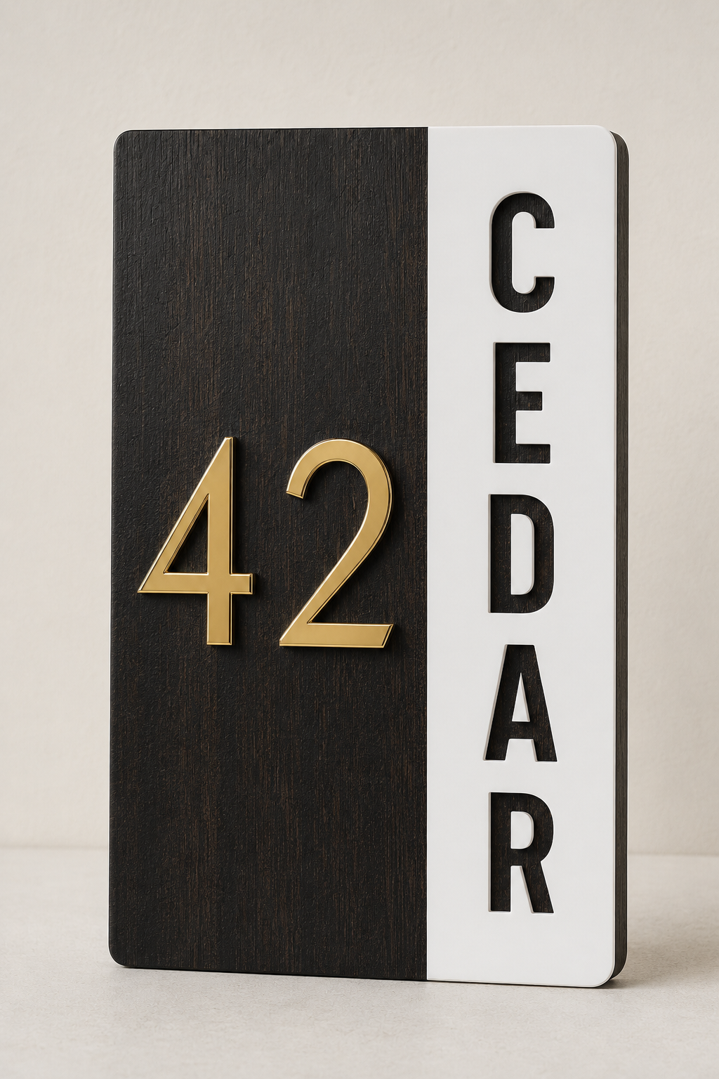 A modern vertical house number sign with a split design: the left half is dark wood grain with raised gold numerals '42', and the right half is white with black vertical letters spelling 'CEDAR'.