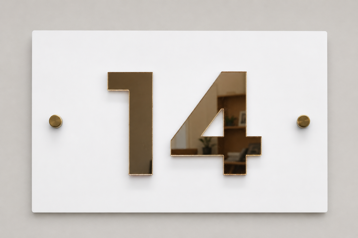 A minimalist white house number sign displaying '14' in large, polished gold-tone numerals, mounted on a light gray wall with two small gold wall anchors.lumorastudio.ie lumora craft studio