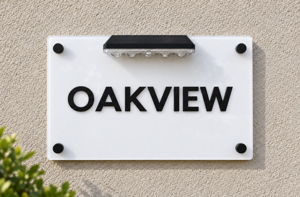 A white acrylic house sign with the word 'OAKVIEW' in bold black letters, mounted on a beige stucco wall with a black solar light above it.lumorastudio.ie lumora craft studio