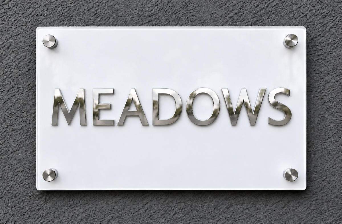 A rectangular white plaque with the word "MEADOWS" in raised metallic silver letters, mounted on a dark textured wall with four silver screws at the corners.lumorastudio.ie lumora craft studio