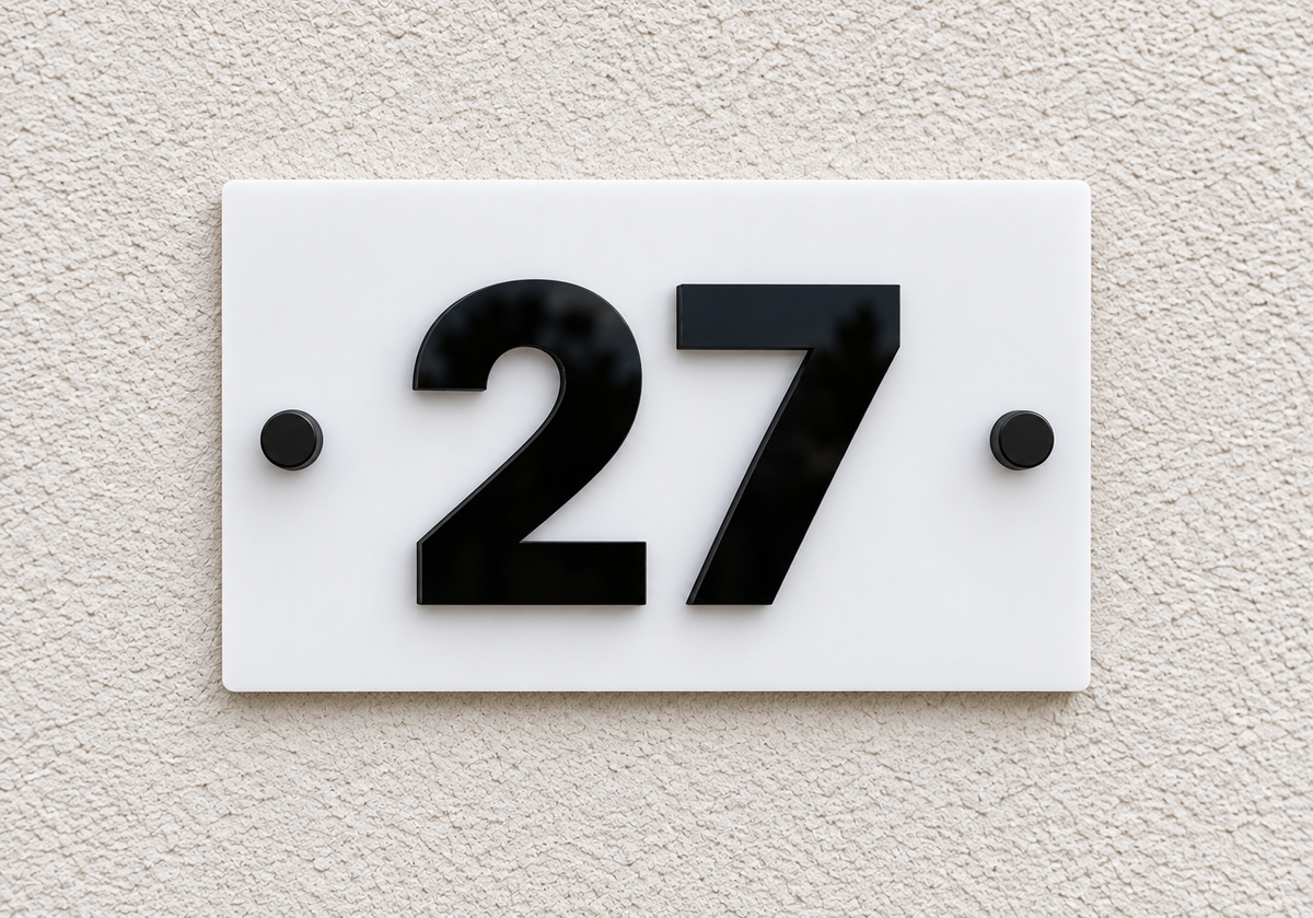 A modern white rectangular house number plaque with bold black numerals '27' mounted on a textured beige stucco wall.lumorastudio.ie lumora craft studio