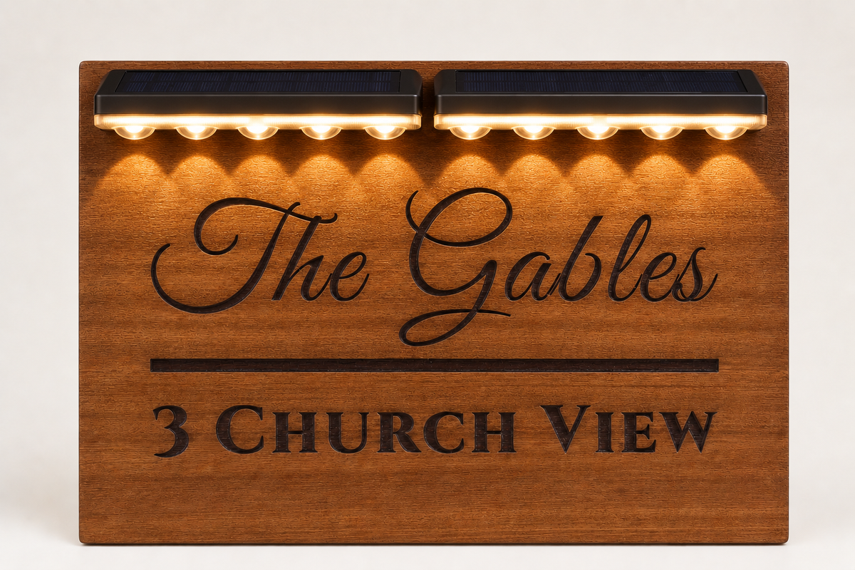 A rectangular wooden sign with warm ambient lighting above it, featuring the engraved text 'The Gables' and '3 CHURCH VIEW'.lumorastudio.ie lumora craft studio