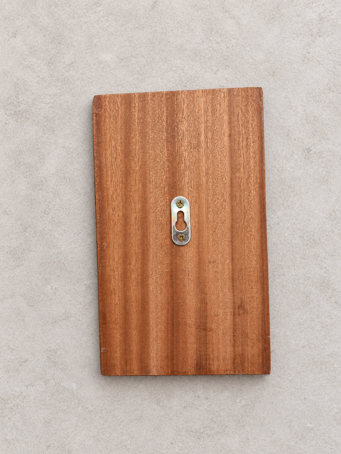 A rectangular wooden board with a warm medium-brown wood grain finish and a small silver metal keyhole detail in the center, shown against a light gray textured background.Lumora Craft Studio, lumorastudio.ie