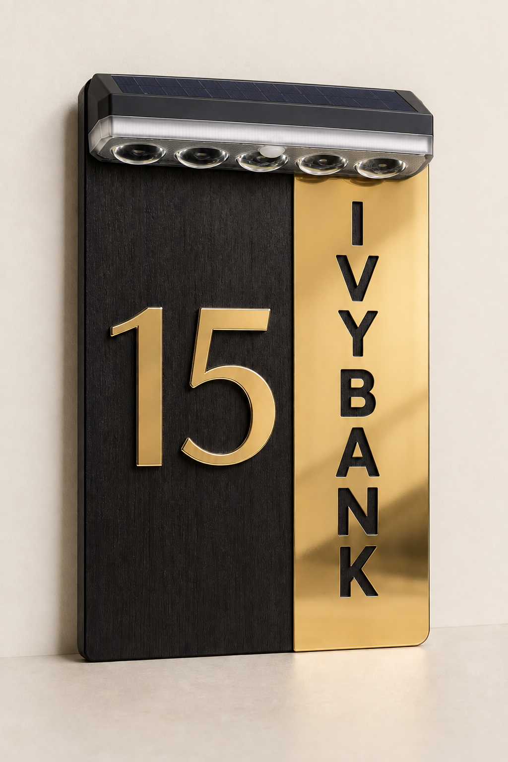 A modern house number sign with a split black and gold design, featuring the number 15 in gold on the left and 'IVYBANK' in black on the right, with an integrated solar light bar at the top, shown against a neutral cream background.